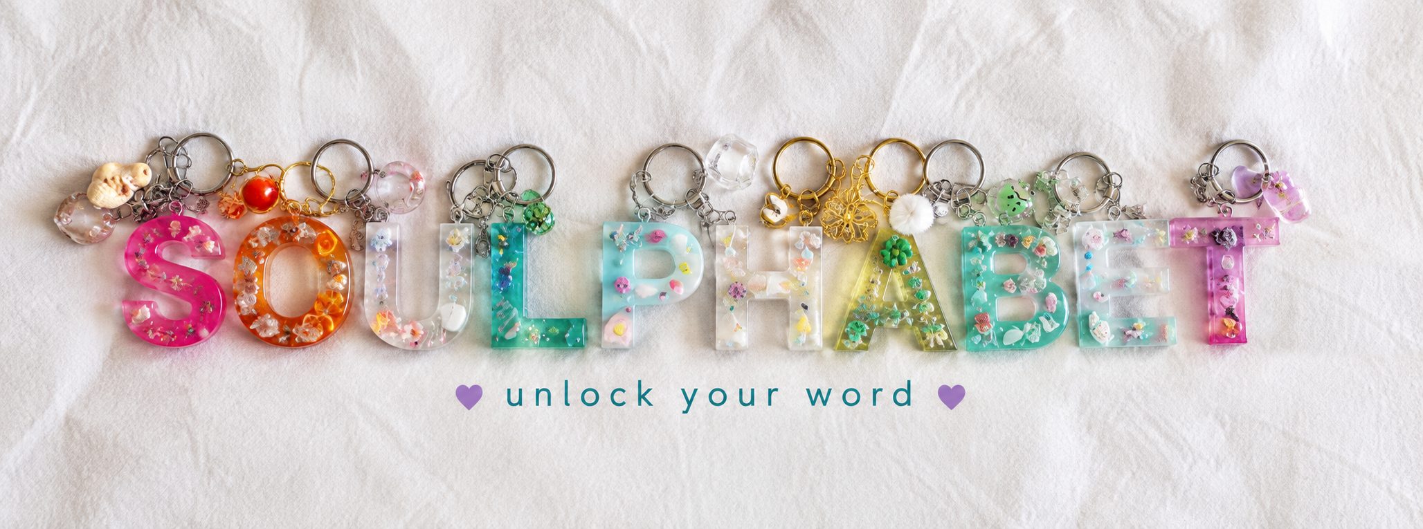 Handmade resin keyrings spelling SOULPHABET on white linen, with the words unlock your word